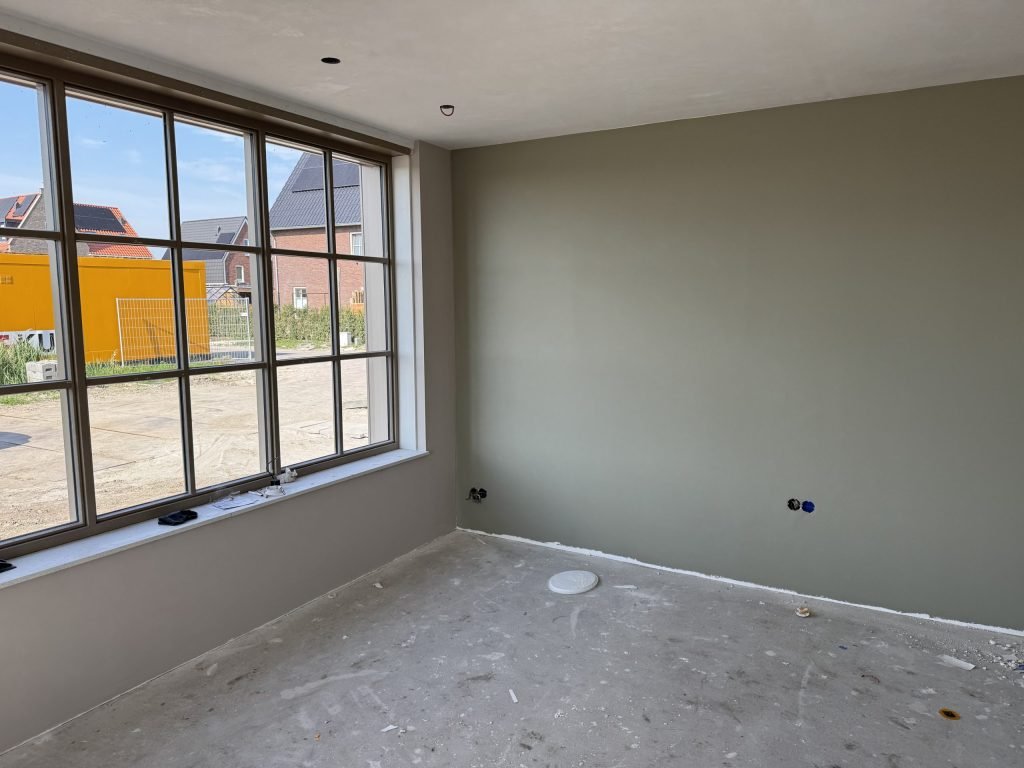 Kamer in een jong huis met een grijsgroen geverfde vlieswand naast een groot raam