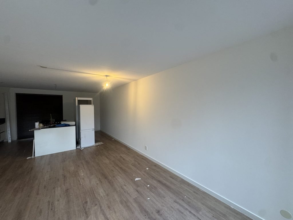 Lange woonkamerwand in een bewoond huis, glad afgewerkt en wit geverfd