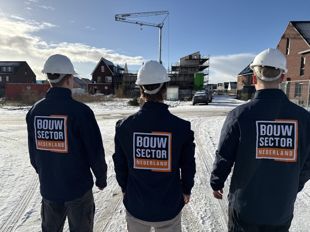 Drie vakmensen van Bouwsector Nederland met witte helm kijken uit over een wijk in aanbouw